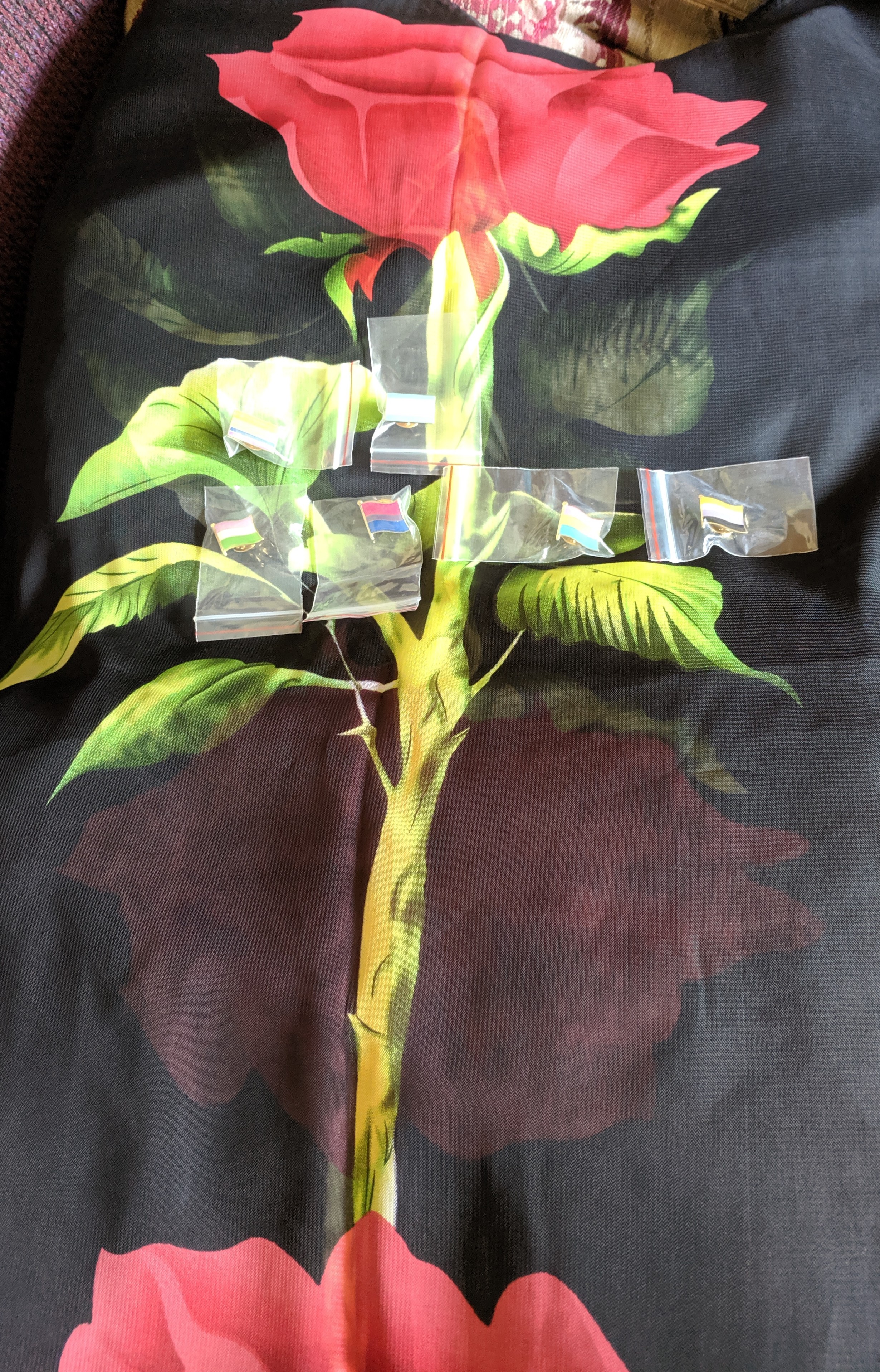 A black diaphanous scarf laid out vertically. A red rose with thorns is printed on it